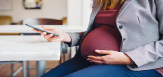 pregnany woman sitting down holding belly in one hand and iphone in other hand